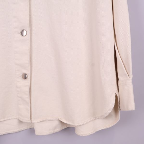 Närbild på nederkant och ärmslut av beige overshirt