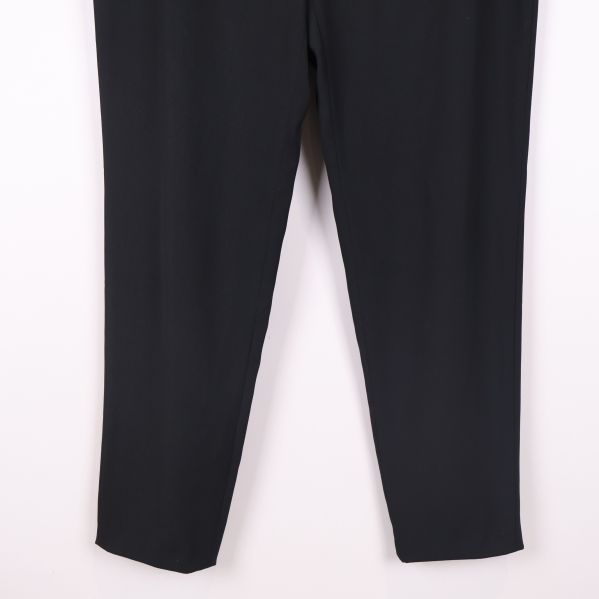 Närbild på benen nertill på svarta byxor mot ljus bakgrund