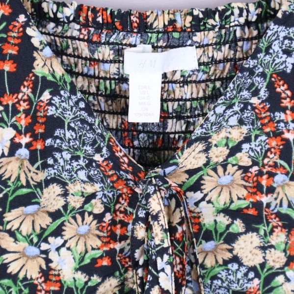 Närbild på halsringning och etikett för blommig blus från H&M