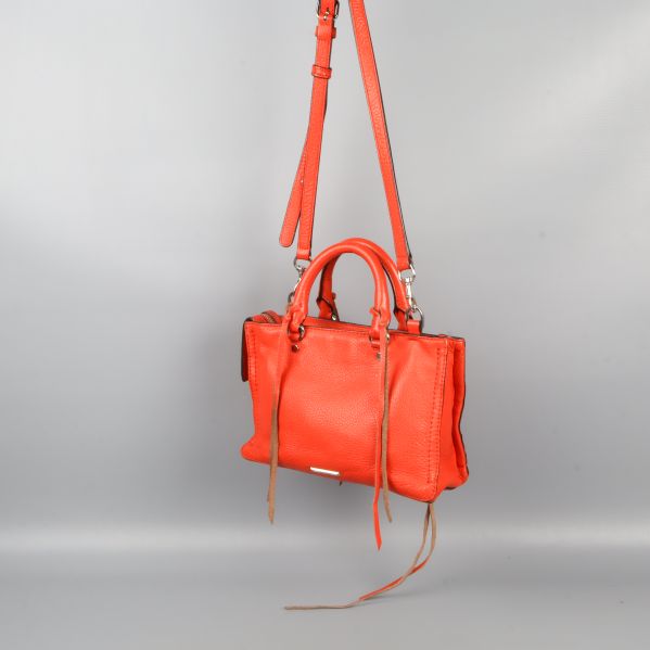 Röd väska hängande i rem mot grå bakgrund