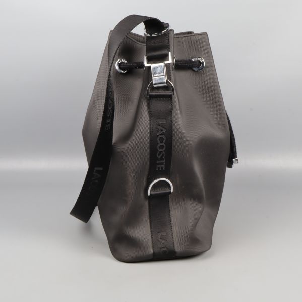 Sidovy av svart bucketbag med Lacoste-text på rem