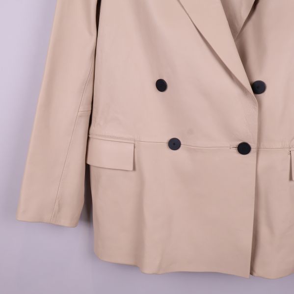 Detaljbild på knappslå och fickor på beige kavaj