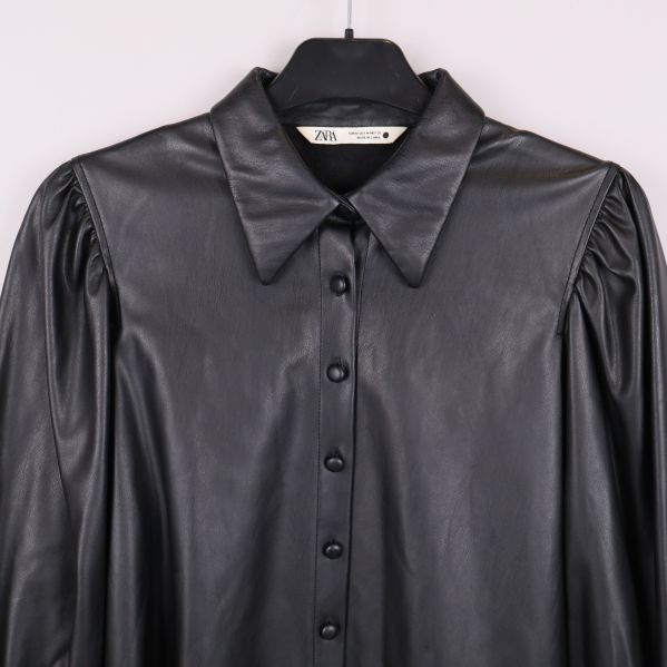 Närbild på krage och knäppning på svart blus i konstläder