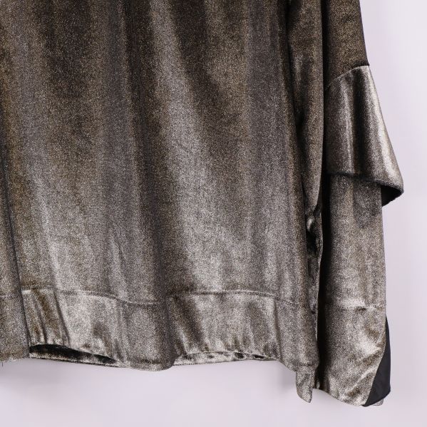 Närbild på nederkant av topp och ärm i glittrigt tyg