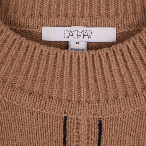 Närbild på Dagmar-etikett vid halsen på beige stickad tröja