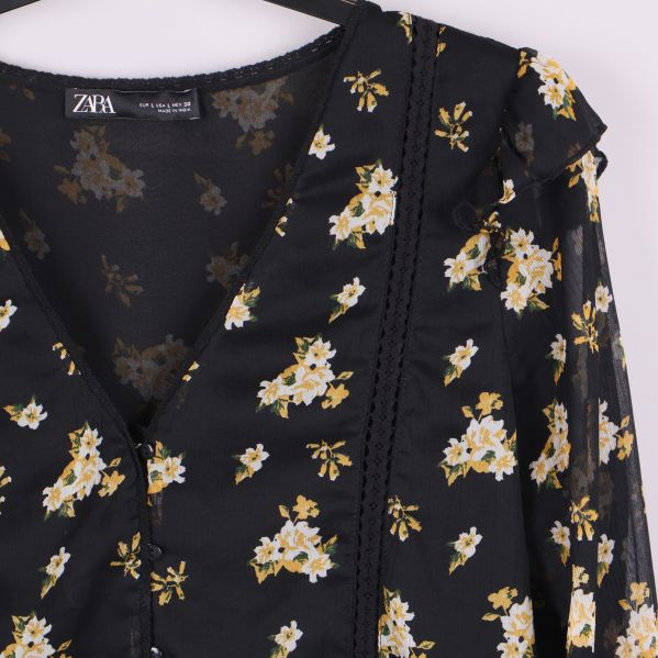 Detalj på framsidan av svart blommig blus