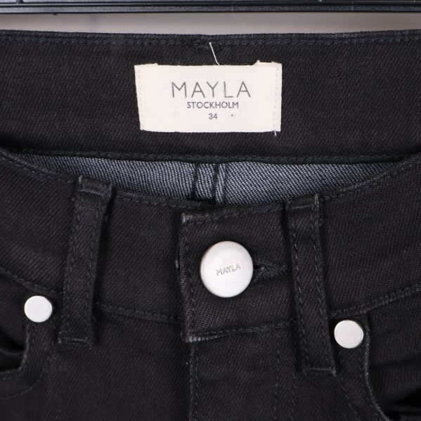 Närbild av Mayla Stockholm etikett och knapp i midjan på svarta jeans