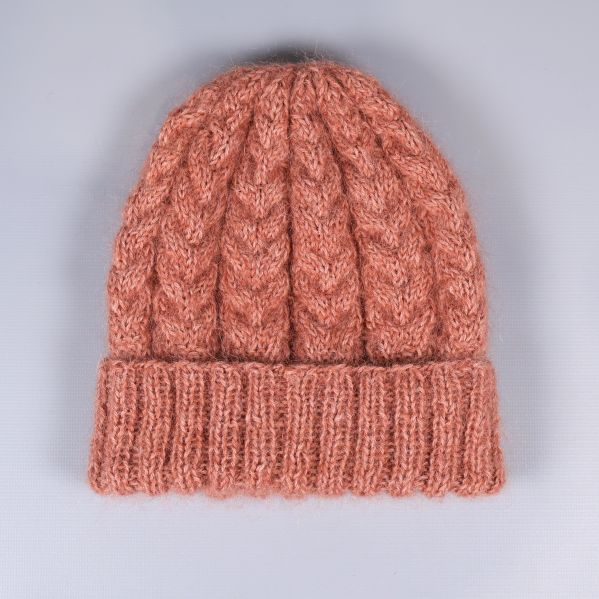 Stickad mössa i kabelmönster platt på grå bakgrund