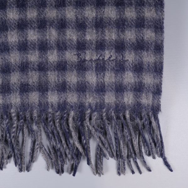 Närbild på broderad logotyp och fransar på rutig halsduk