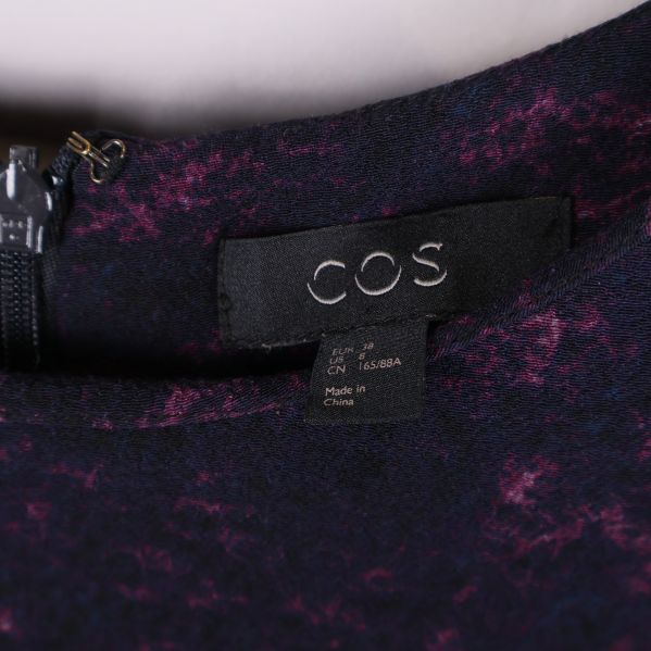 Närbild på COS-logga i halsen på klänningen