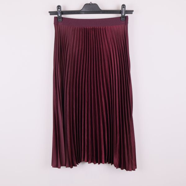 Vinröd plisserad kjol på galge mot vit bakgrund