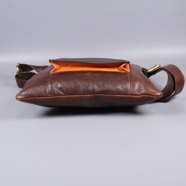 Brun axelremsväska liggande med orange foder synligt