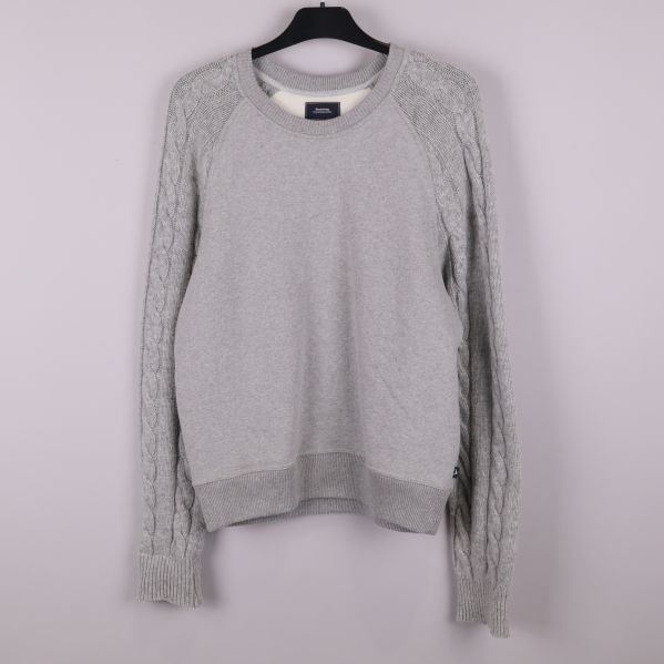 Grå stickad tröja på galge mot ljus bakgrund