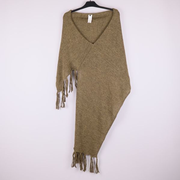 Stickad brun poncho med fransar på galge mot ljus bakgrund