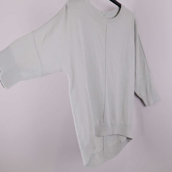 Stickad tröja i ljusgrått fotad i profil