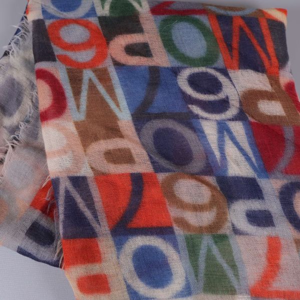 Närbild på mönstrat tyg i blått, rött och grönt med bokstäver och fransar