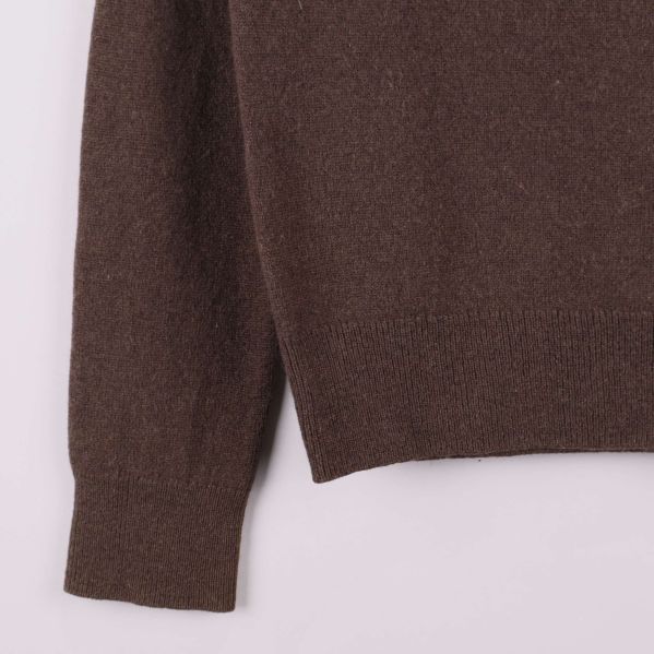 Stickad mudd och nederkant på brun tröja i närbild