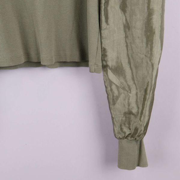 Närbild på ärmslut i glansigt tyg och mudd på olivgrön tröja