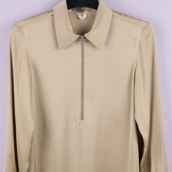 Närbild framtill på beige blus med dragkedja och krage