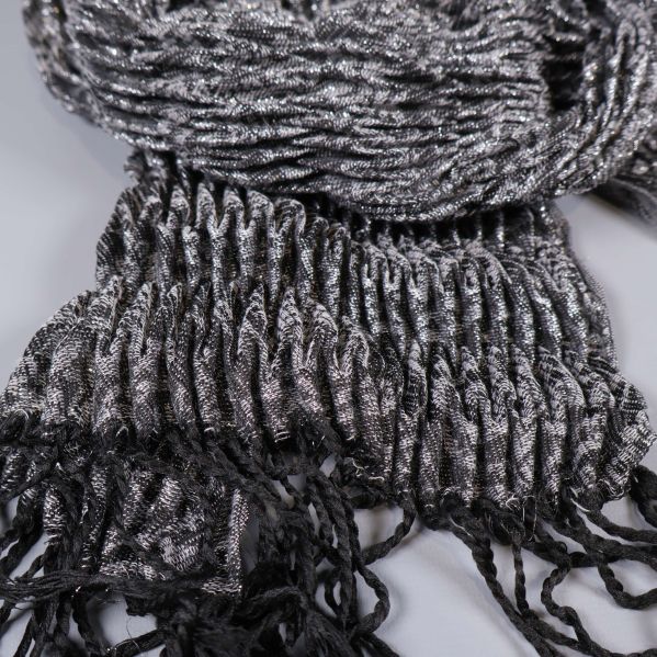 Närbild på stickad struktur och fransdetaljer i svart och silvergrått