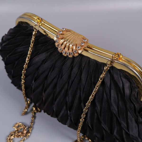 Närbild på guldigt snäckspänne och kedjerem på svart väska