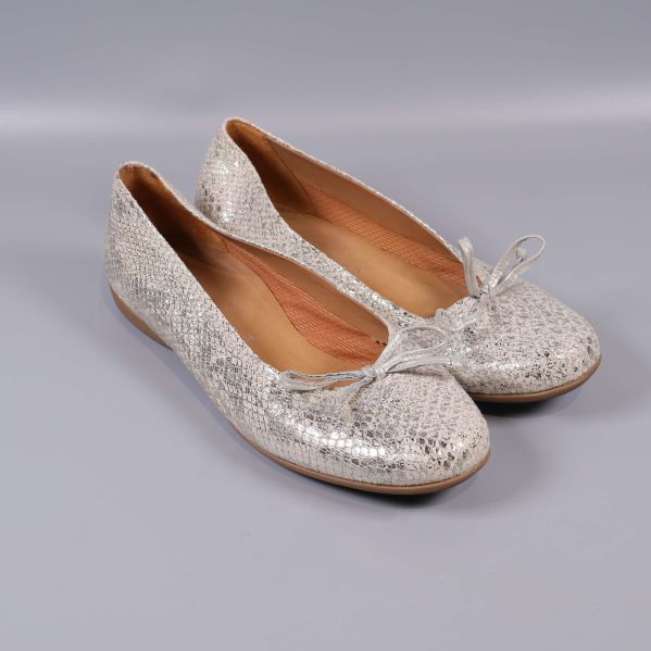 Ett par ballerinaskor med metallisk yta och rosett