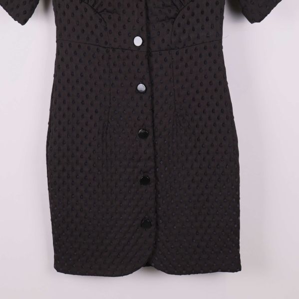 Närbild på nederdelen av svart klänning med knappslå