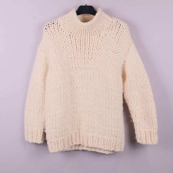 Framsidan av naturvit grovstickad polotröja på galge