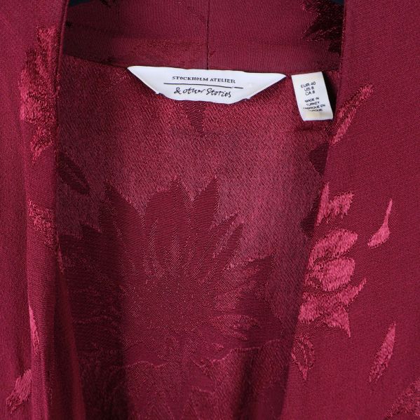 Närbild på krage och etikett i vinröd mönstrad klänning