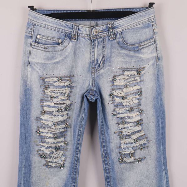 Närbild av slitningar och paljettdetaljer framtill på jeans