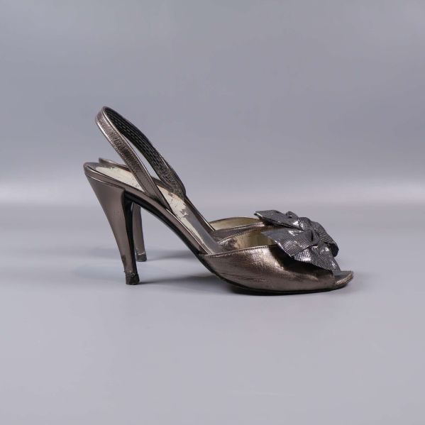 Sida av klackskor med metallisk yta och rosett