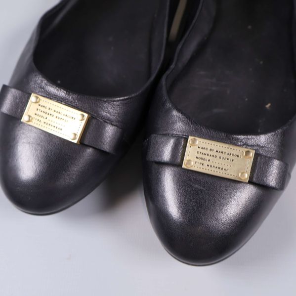 Närbild på rosett och guldfärgad skylt framtill på skorna