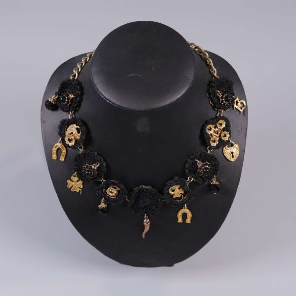 Halsband närbild med svarta blommor och berlocker