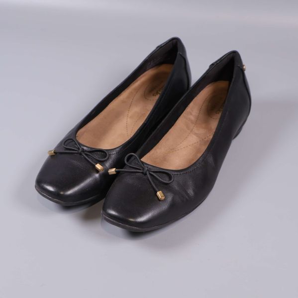 Svarta ballerinaskor med rosett och gulddetalj sedd snett framifrån