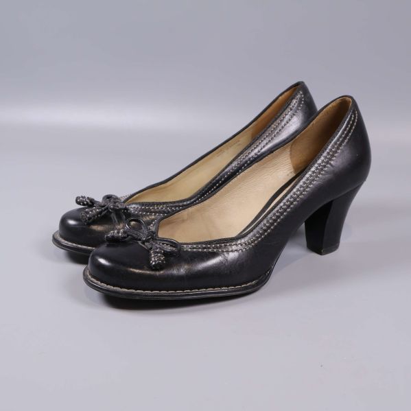 Pumps i svart läder med rosett och vit stickning