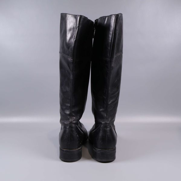 Baksida på höga svarta stövlar mot grå bakgrund