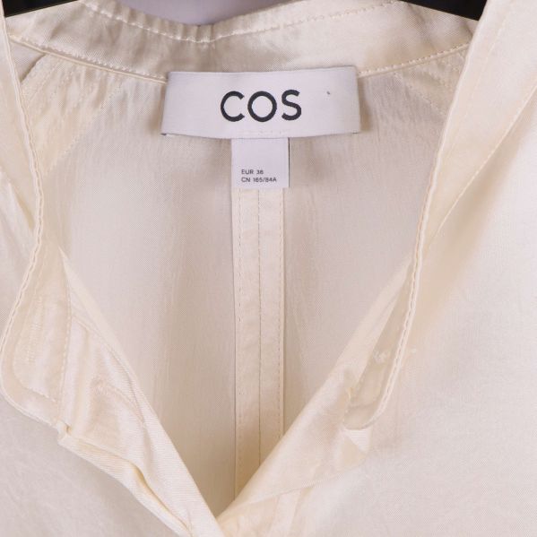 Närbild på COS-logotyp i blusens krage