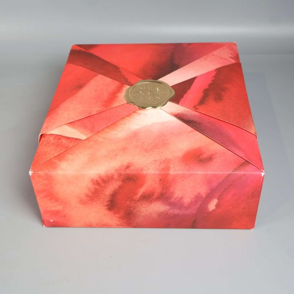 Toppvy över presentbox med rödrosa akvarellmönster och gulddetalj