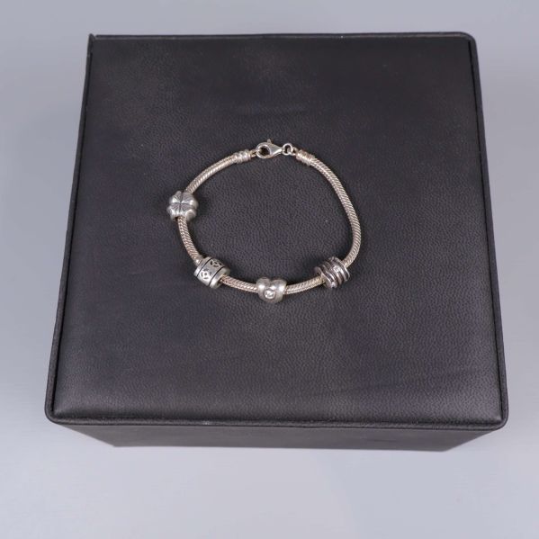 Silverfärgad armbandslänk med berlocker på svart underlag