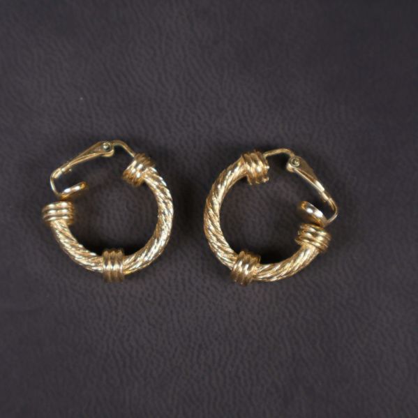 Guldfärgade örhängen visade uppifrån mot svart yta