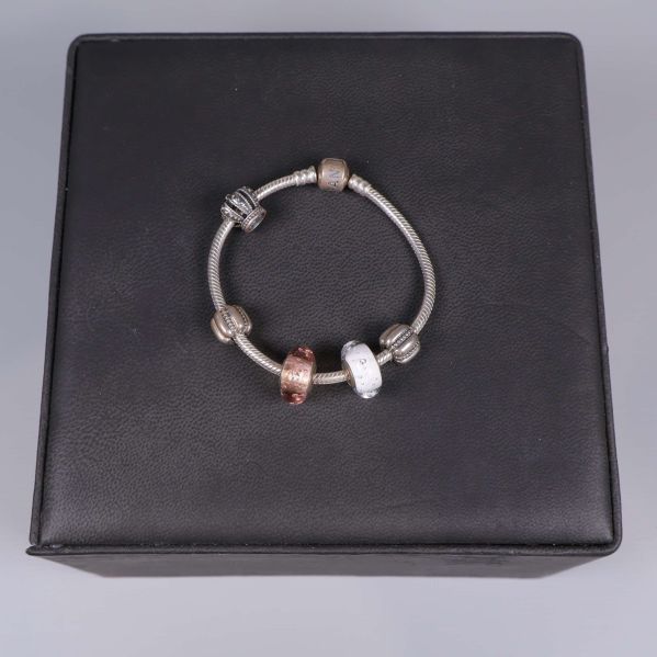 Armband med flera metallberlocker placerat på svart underlag