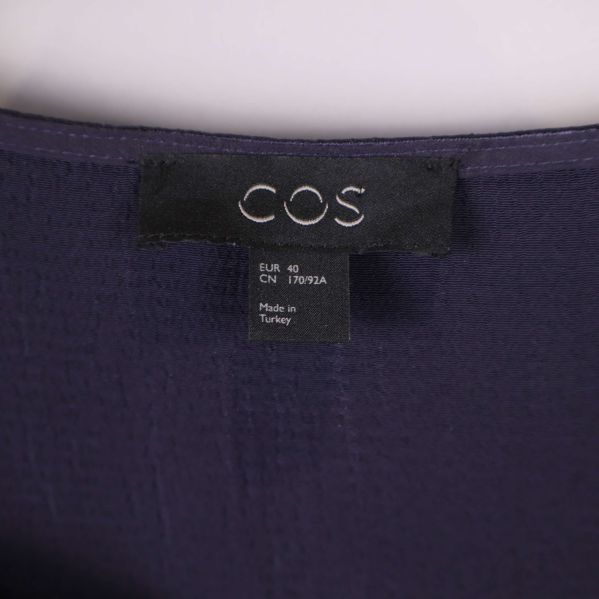 Närbild på COS-logotyp i nacklinning på klänning