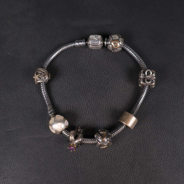 Pandora armband med berlocker liggande på svart underlag