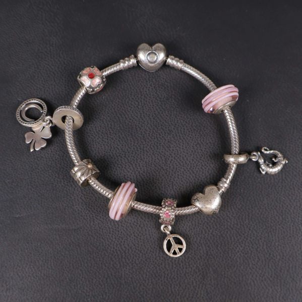 Närbild på armband med silver- och rosa berlocker liggande på svart underlag