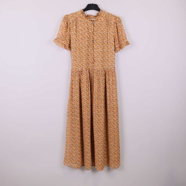 Lång blommig klänning med volanger på galge mot ljus bakgrund