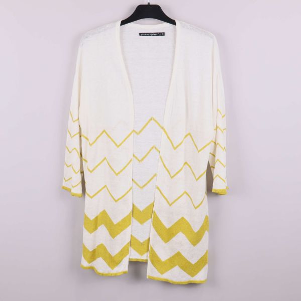 Framsida av naturvit kofta med gult zigzagmönster på galge