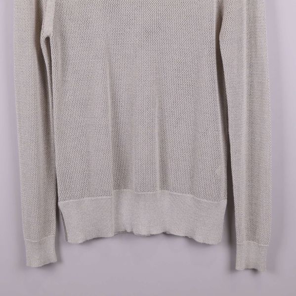 Närbild på tröjans nederdel och ärmslut i ljusbeige stickning