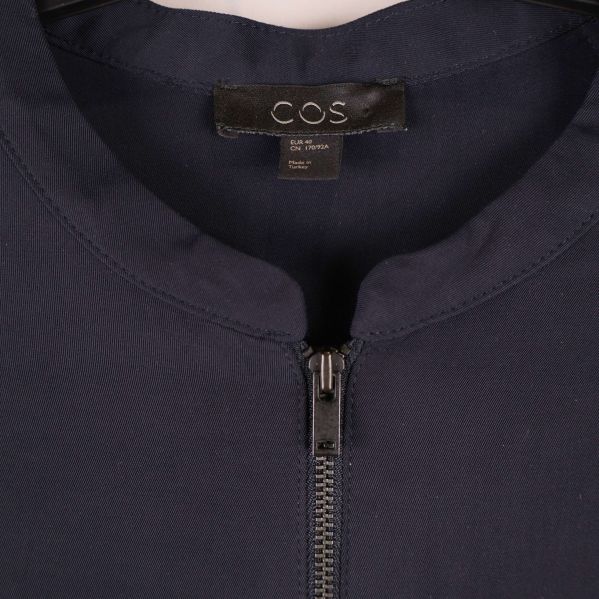 Närbild på halsringning och dragkedja samt COS-märke