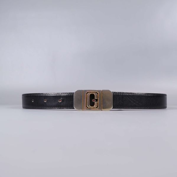 Svart bälte med mässingsfärgat spänne på plan yta