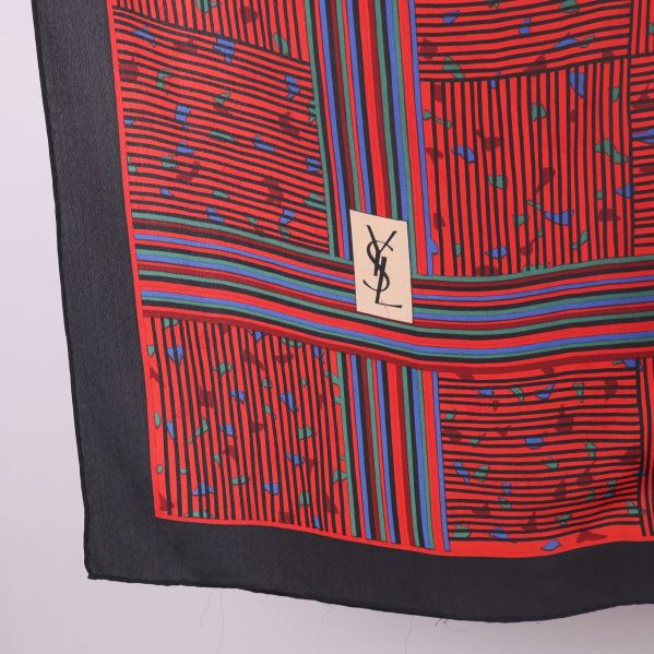 Närbild på YSL-logga mot rött och randigt mönster